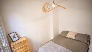 Un dormitorio con cama, mesita de noche, aparador de mimbre y lámpara colgante.