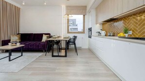 A modern kitchen with white cabinets, a herringbone backsplash, and a dining area with a purple sofa and a wooden table.