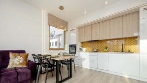 A modern kitchen with white cabinets, a herringbone backsplash, and a dining area with a purple sofa and black chairs.