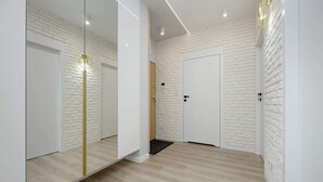 A hallway with white brick walls, a wooden floor, and a large mirror with a gold frame.