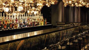 A bar area with a marble countertop, numerous bottles of liquor, and a row of chairs.