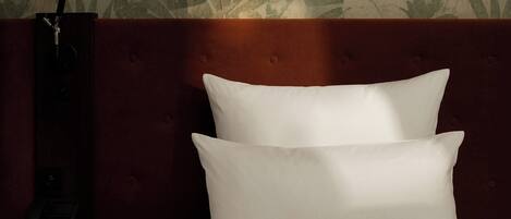 A bed with white pillows and a dark headboard, a bedside lamp, and a telephone on a wooden nightstand.