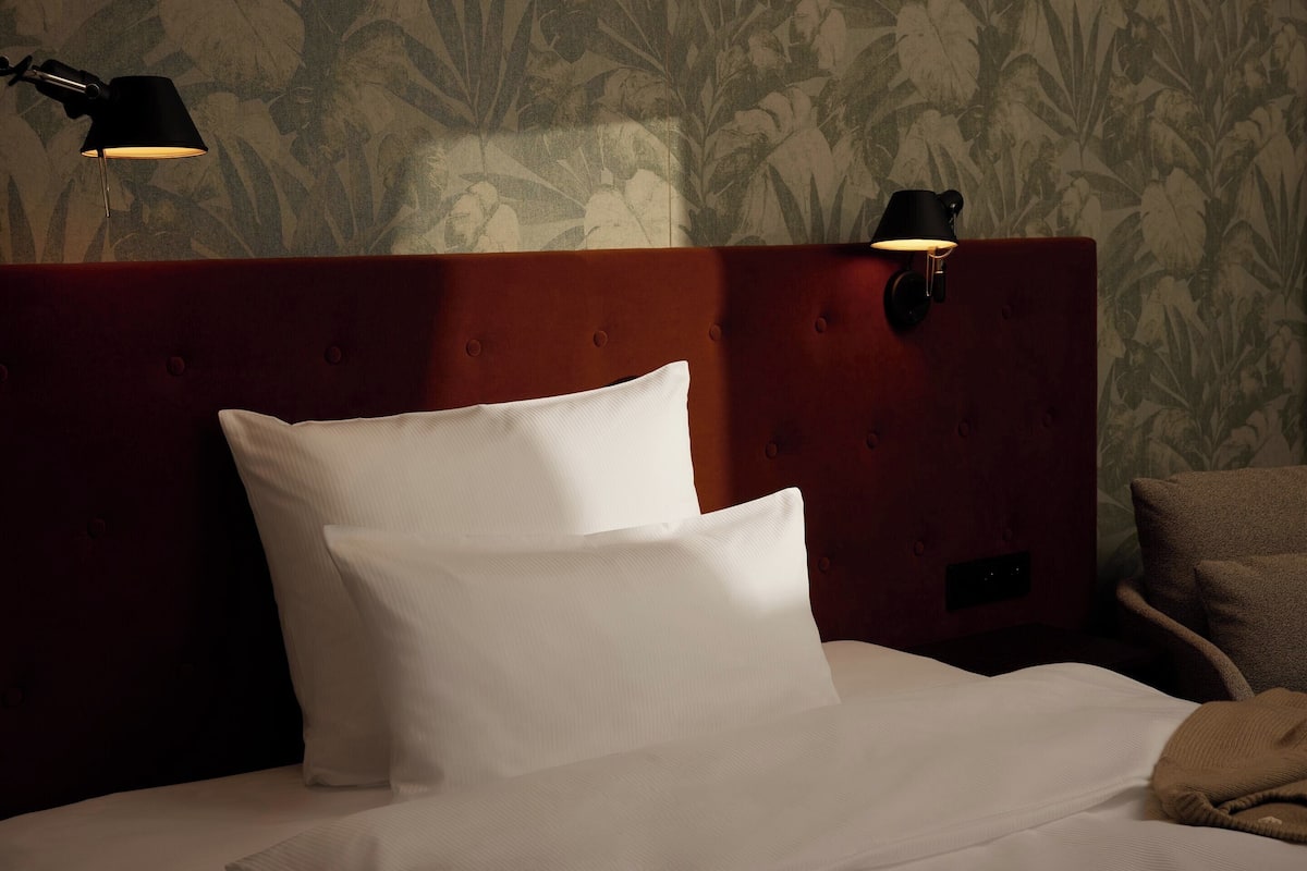 A neatly made bed with white linens and two black wall-mounted lamps on a wooden headboard.