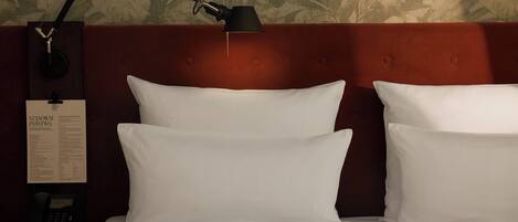 Cama bem arrumada com lençóis brancos, cabeceira marrom escura e abajur preto.
