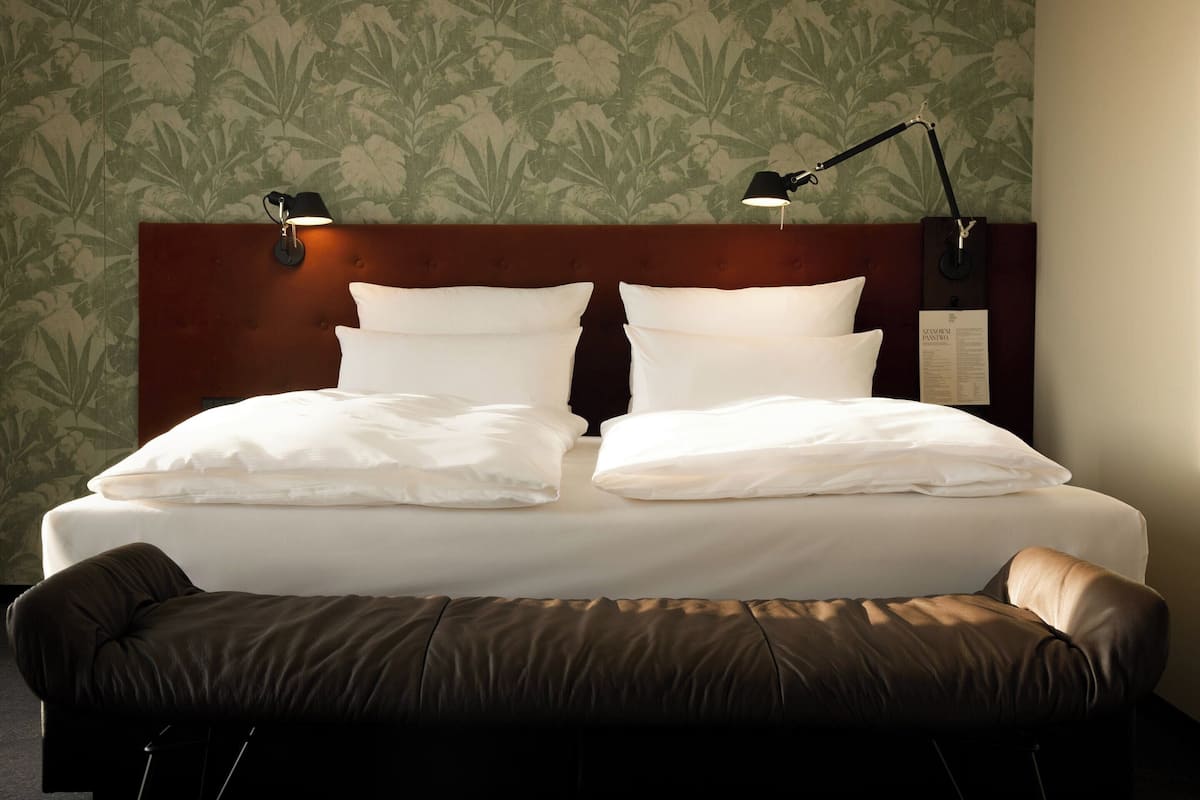 A neatly made bed with two pillows and a headboard with two wall-mounted lamps.