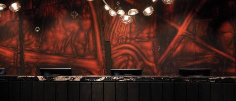Una zona de bar con mostrador de madera oscura y un mural abstracto rojo de fondo.