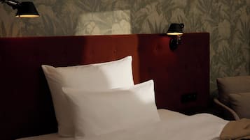 A neatly made bed with white linens and two black wall-mounted lamps on a wooden headboard.