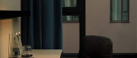 Una habitación de hotel moderna con una butaca de cuero oscura, un escritorio con lámpara y una ventana con cortinas.