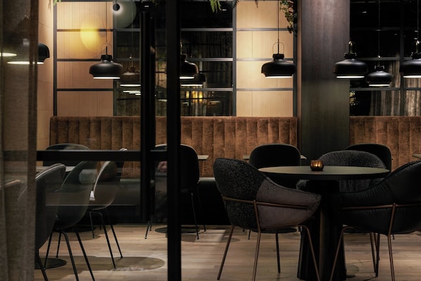 Un intérieur moderne avec des tables rondes et des chaises noires, des murs recouverts de panneaux en bois et des luminaires suspendus.