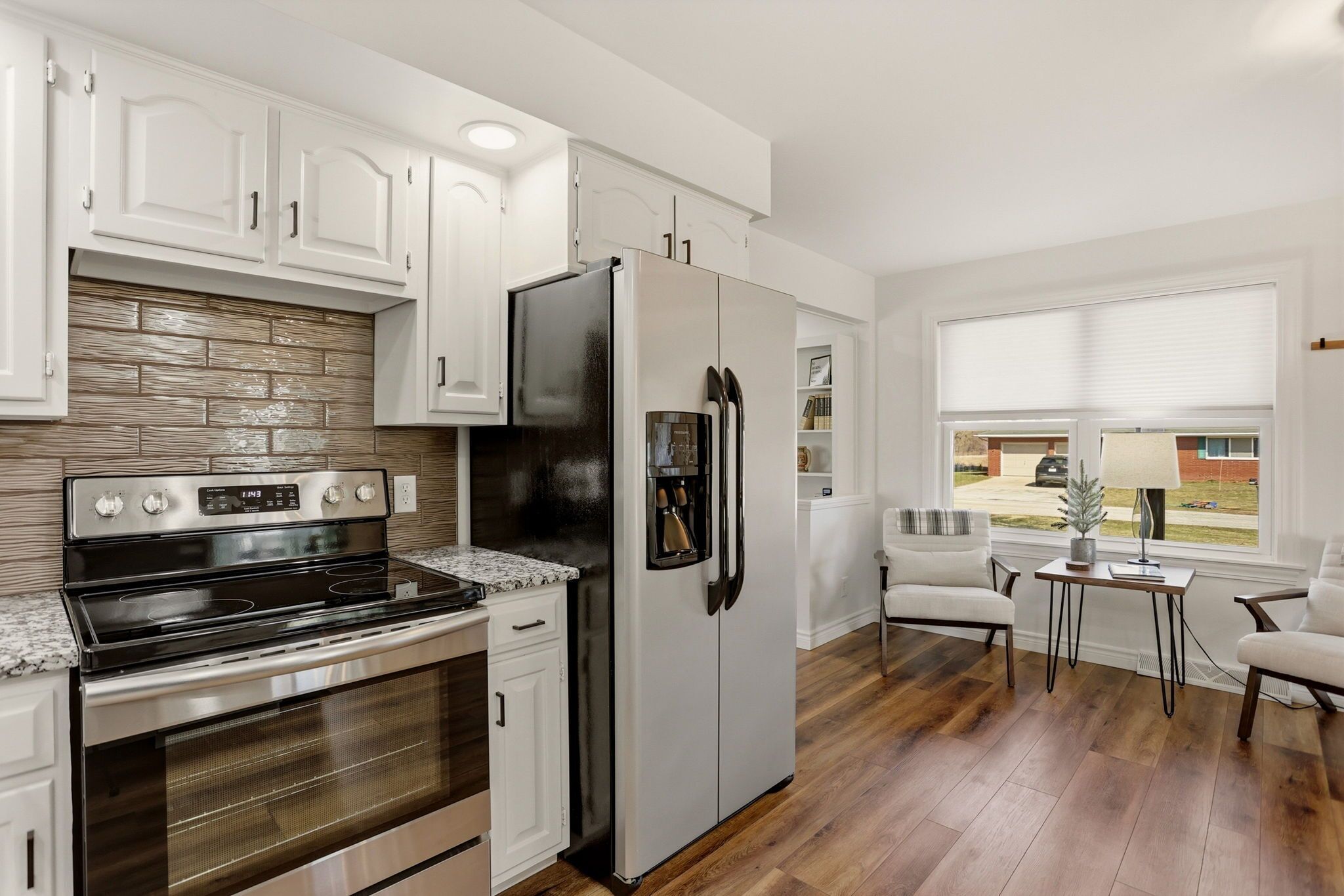 A modern kitchen with white cabinets, stainless steel appliances, and a brick backsplash.