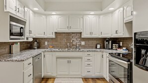 A modern kitchen with white cabinets, a granite countertop, a built-in microwave, and a stainless steel oven.