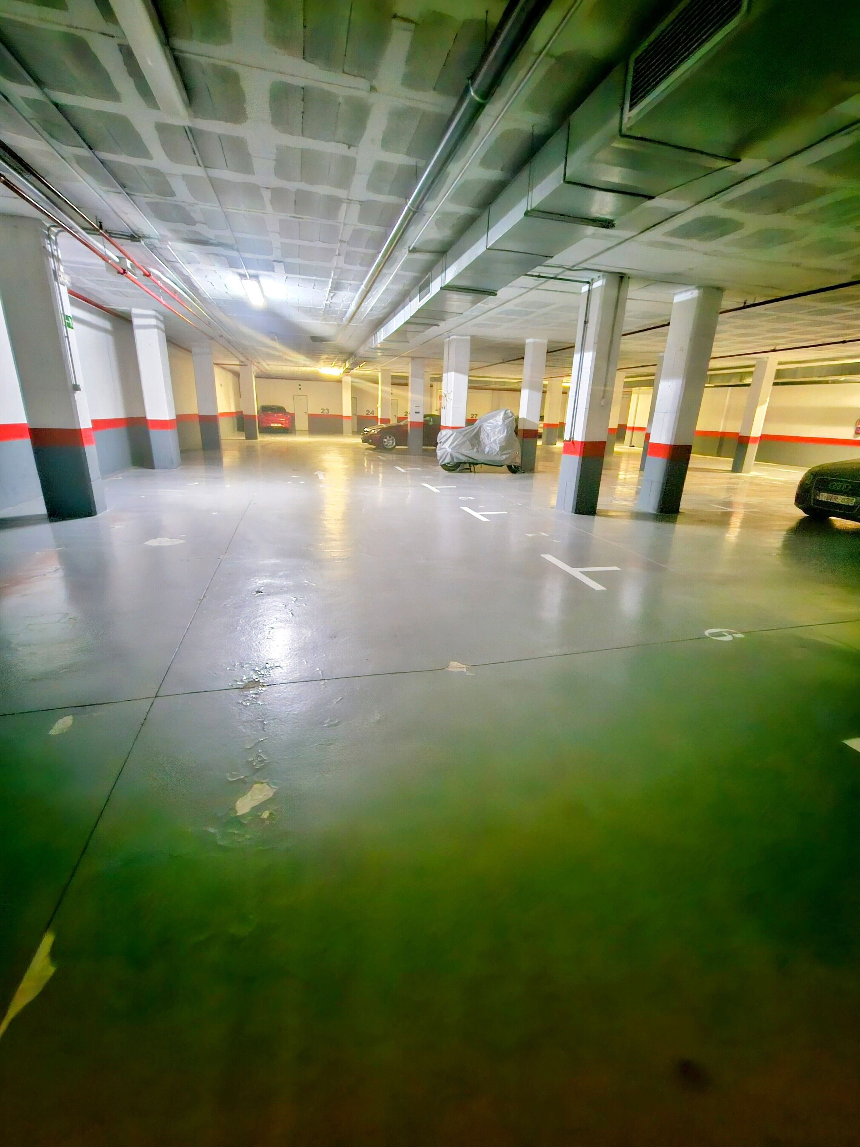 Un estacionamiento de varios niveles con pilares de hormigón y flechas direccionales en el suelo.