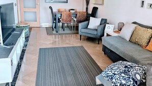 Een moderne woonkamer met een grijze bank, een eettafel met stoelen en een tv op een dressoir.