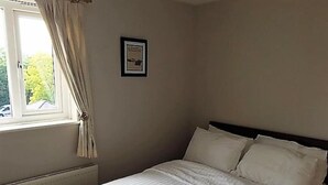A bedroom with a bed, a window with curtains, a radiator, and a framed picture on the wall. - Beautiful Penthouse Apartment (Shepperton)