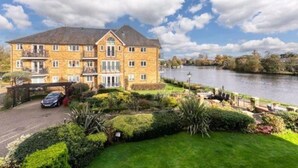 A multi-story hotel with a stone facade, a parking area, and a river view. - Beautiful Penthouse Apartment (Shepperton)