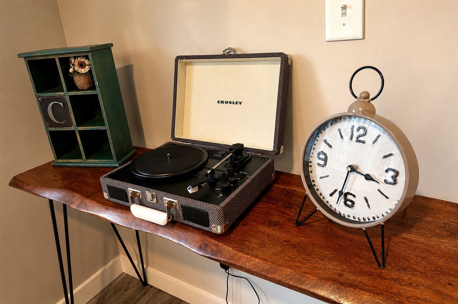 Een oud model platenspeler in een hoes, met een klok ernaast op een houten tafel.