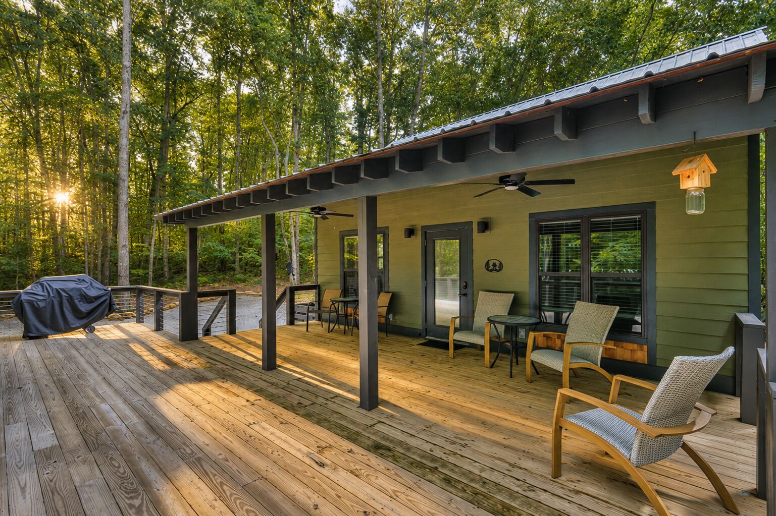 Eine überdachte Terrasse mit Holzboden, Sitzgelegenheiten im Freien und einem Grill.