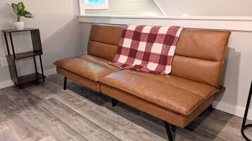A brown leather sofa with a checkered throw blanket, positioned against a wall with a window above.