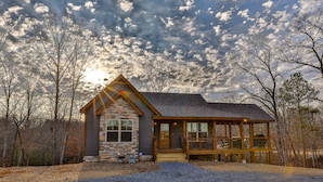 A cabin with a stone facade, large windows, and a wooden deck.