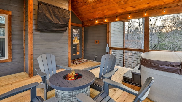 A covered outdoor area with a fire pit table, two Adirondack chairs, and a large tub.