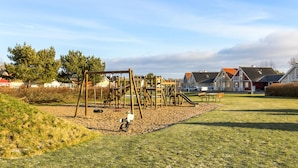 Un parc infantil amb estructures de fusta, una panxa de darrera i cases al fons.