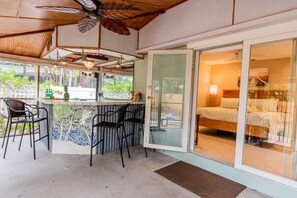 A room with a bed, a glass door leading to a balcony, and a bar area with chairs and a counter. - 791 Sunset Cottage · NEW Heated Pool/Spa (Naples)
