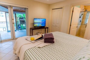 A hotel room with a bed, a television, a tray with breakfast items, and a bathroom with a shower. - 791 Sunset Cottage · NEW Heated Pool/Spa (Naples)