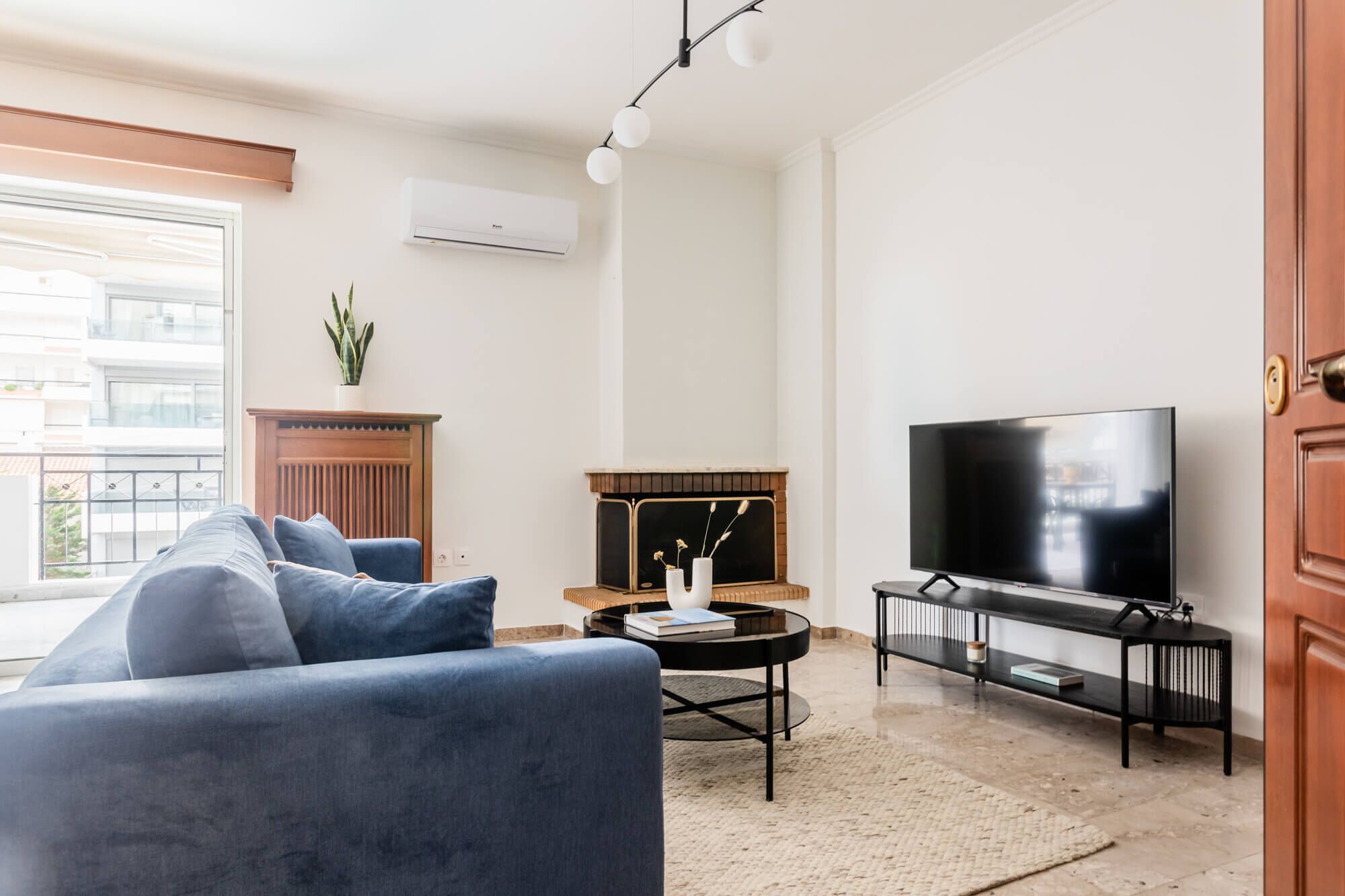A modern living room with a sofa, a fireplace, a TV, and a large window.
