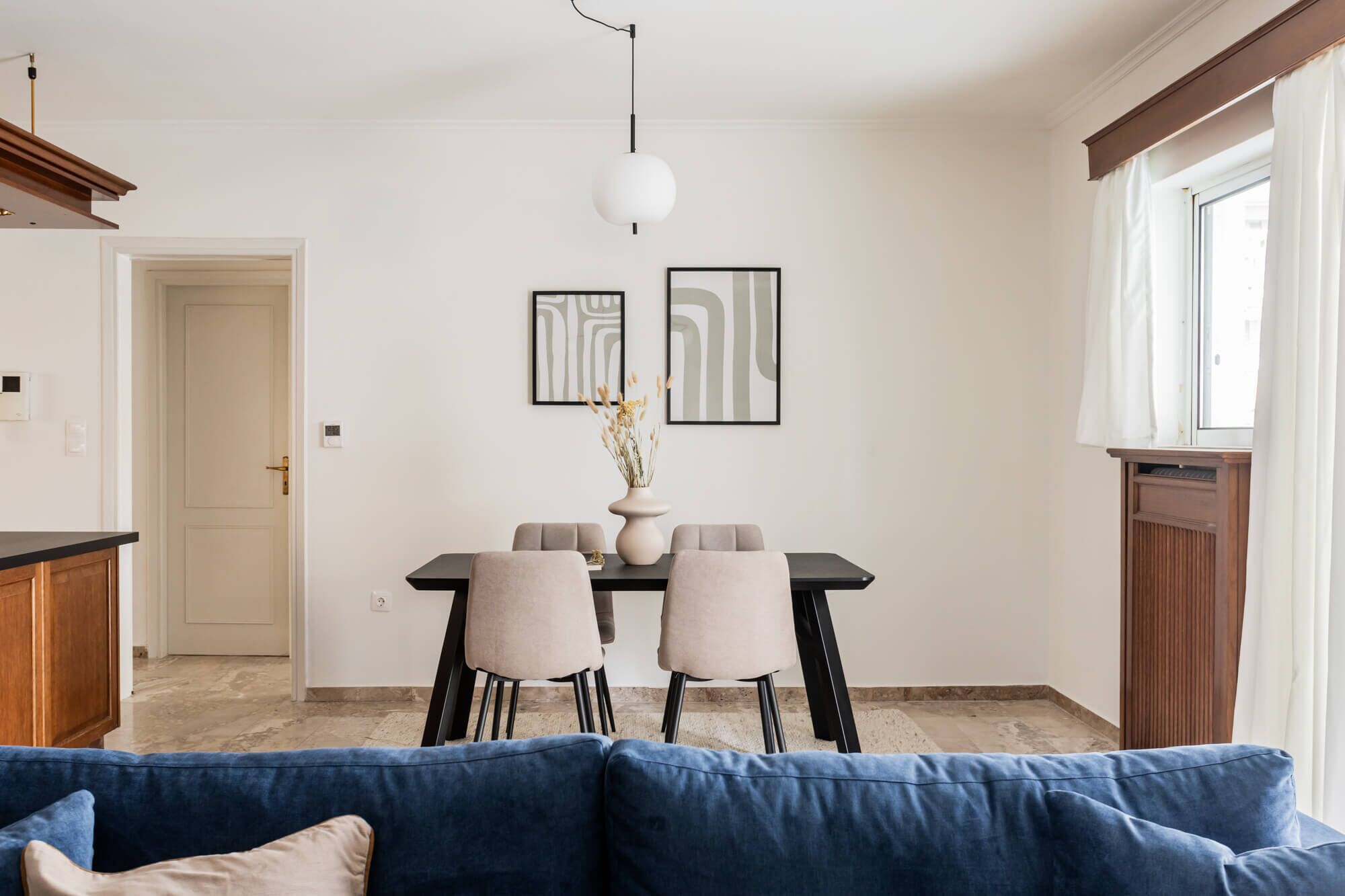 Een moderne woonkamer met een blauwe bank, een eethoek met twee stoelen en een tafel, en een keuken met houten kasten.