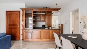 A modern kitchen with wooden cabinets, a built-in oven, and a dining area with a table and chairs. - Faliro Sunlit 3BR Apartment (Palaio Faliro)
