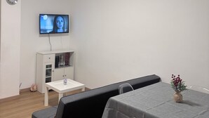 A modern room with a white sofa, a small table with a vase, a television on the wall, and a ceiling light. - ApartUry at TorinoMetroStop (Torino)