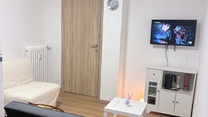 A modern room with a bed, a small table with a vase, a television, a radiator, and a cabinet with kitchen items. - ApartUry at TorinoMetroStop (Torino)
