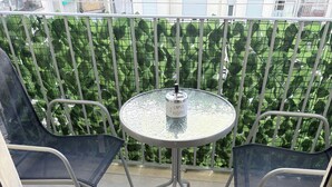 A balcony with a glass table and two chairs, a metal railing, and a green hedge in the background. - ApartUry at TorinoMetroStop (Torino)
