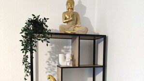 Una estantería metálica negra de varios niveles con diversos objetos decorativos, incluyendo una estatua de Buda, una planta y varios jarrones.
