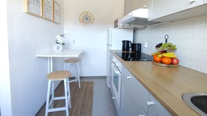 Una cocina compacta con armarios blancos, encimera de madera, un reloj y una exhibición de frutas.