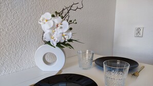 Una mesa dispuesta con platos negros, copas de cristal transparente y un jarrón blanco con flores blancas.