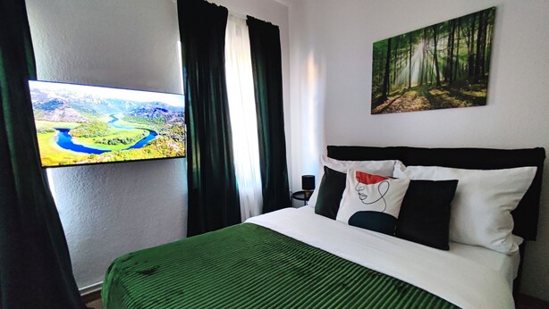 Una habitación de hotel con una cama, un cuadro de un bosque, un cuadro de un paisaje y una ventana con cortinas.