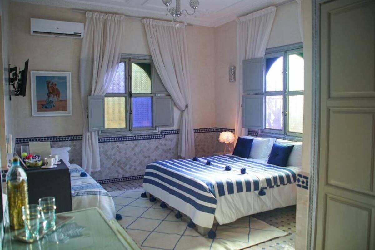 A hotel room with two beds, a desk, a chair, a table with glasses, and a window with curtains.