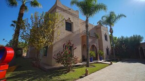 A building with a traditional architectural style, featuring arched doorways and a courtyard with palm trees and a small garden. - Villa Atika Maison d'hôtes & SPA (Marrakech)