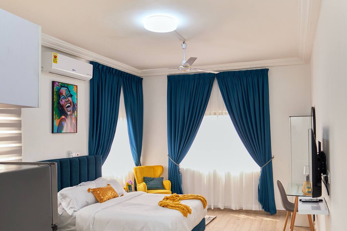 Une chambre moderne avec un lit, une chaise, un bureau et un ventilateur de plafond.