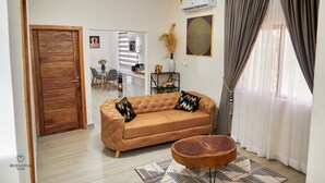 A living room with a brown sofa, a round wooden coffee table, and a patterned rug. - Red Lotus Oasis (Accra)