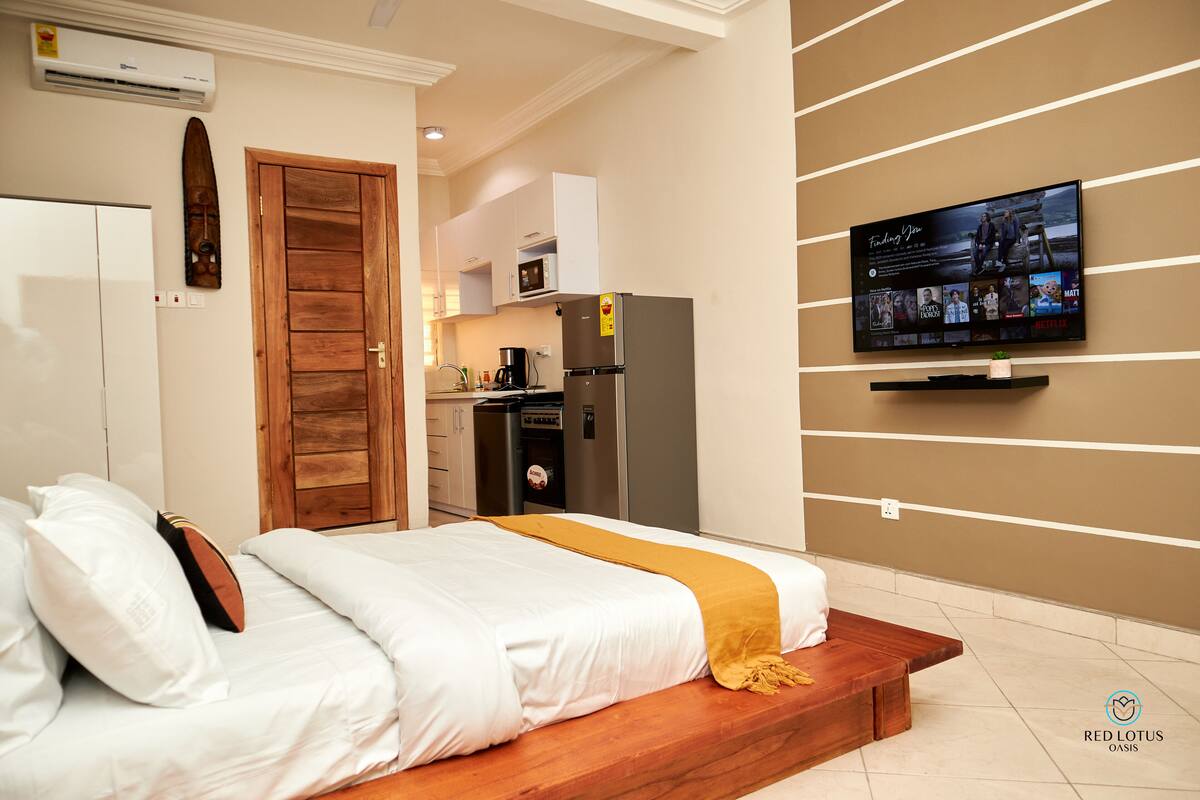 Une chambre d’hôtel moderne équipée d’un lit, d’un banc en bois, d’une télévision, d’une kitchenette et d’une télévision fixée au mur.