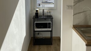 Et lille køkken med et vindue, en mikroovn, en sort hylde og en vask.