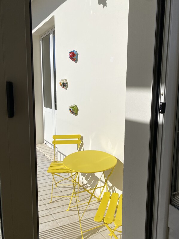 A yellow table and chairs set on a balcony with a white wall and a door in the background.