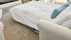 Ein Schlafzimmer mit einem Bett, einem Fernseher, einem Schreibtisch und einem Fenster mit Vorhängen.