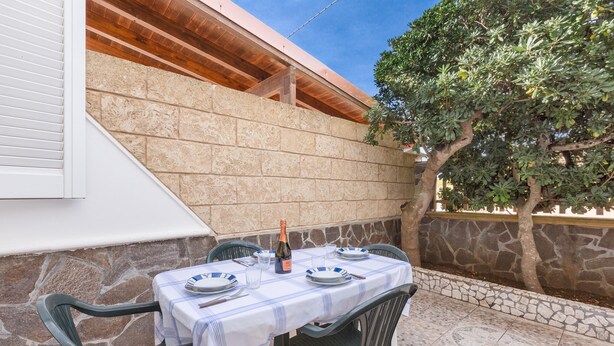 Un área de comedor al aire libre con una mesa preparada para cuatro personas, rodeada de muros de piedra y un árbol.