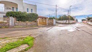 Una calle residencial con un acceso cerrado, una casa moderna con balcón y un cielo despejado.