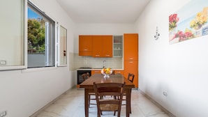 Una cocina compacta con armarios color naranja, una mesa de comedor con cuatro sillas y una ventana con vistas a árboles.