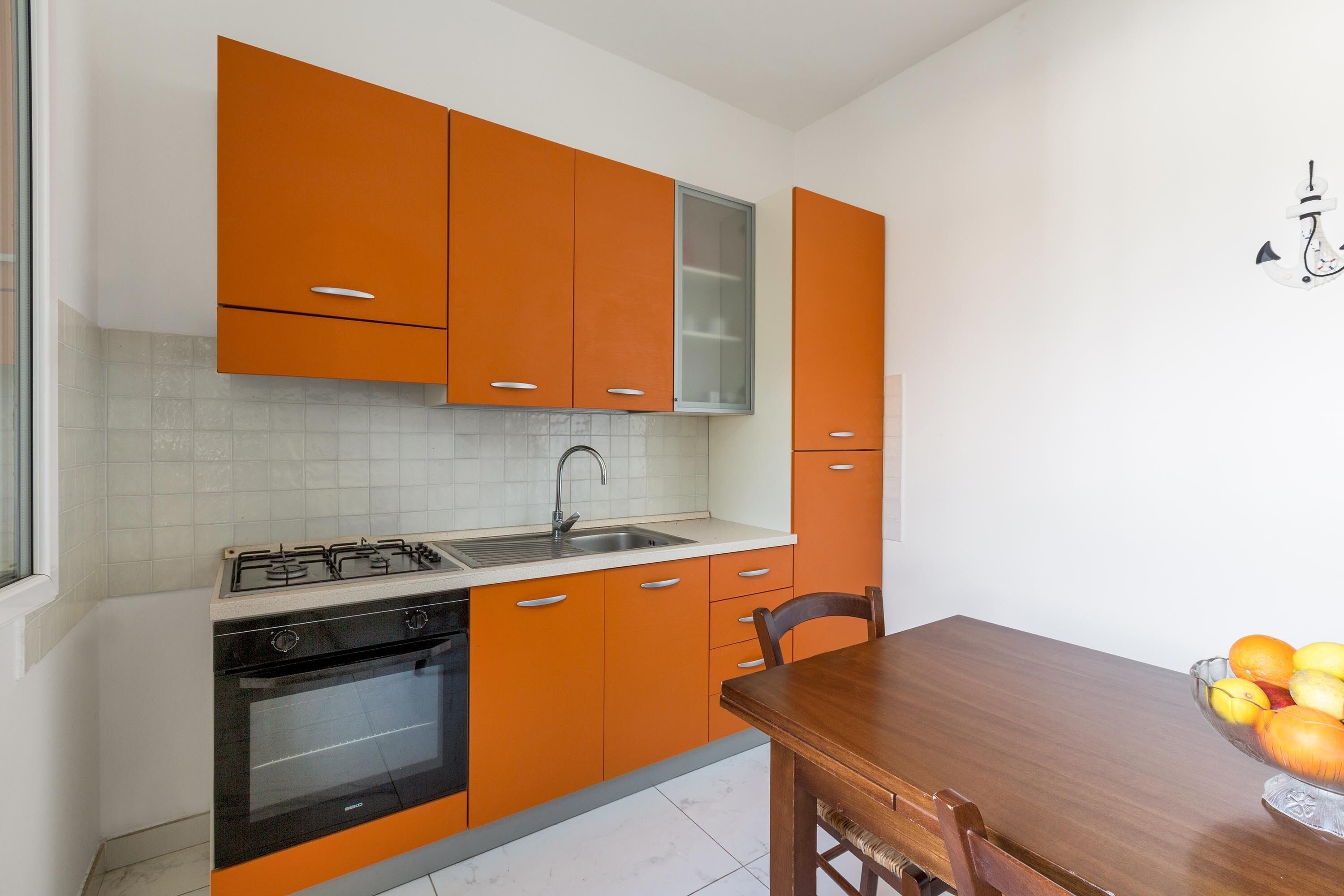 A kitchen with orange cabinets, a stove, and a sink.