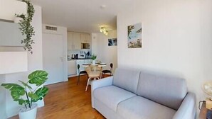 Una sala de estar con un sofá gris, una mesa de comedor con sillas y una cocina al fondo.